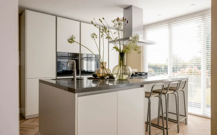 Woonkeuken met grote glazen vazen en bloemen op het zwart marmeren werkblad van het kookeiland.