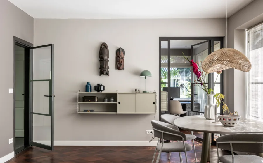 Klein wandkastje met open vakken voor keramiek en sculpturen van natuurlijke materialen en maskers op de wand.