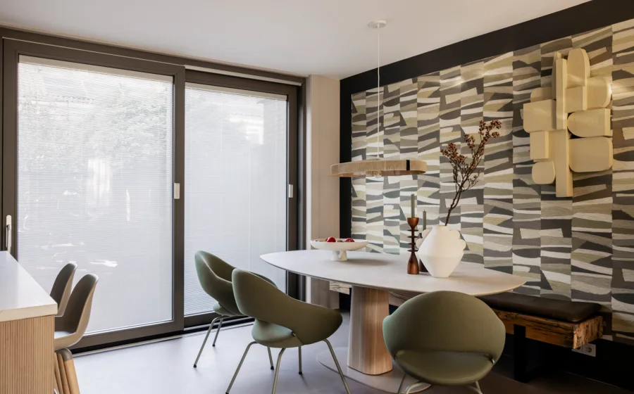 Eethoek met behang met print in groen en grijstinten, ronde tafel en lichtgroene kuipstoelen.