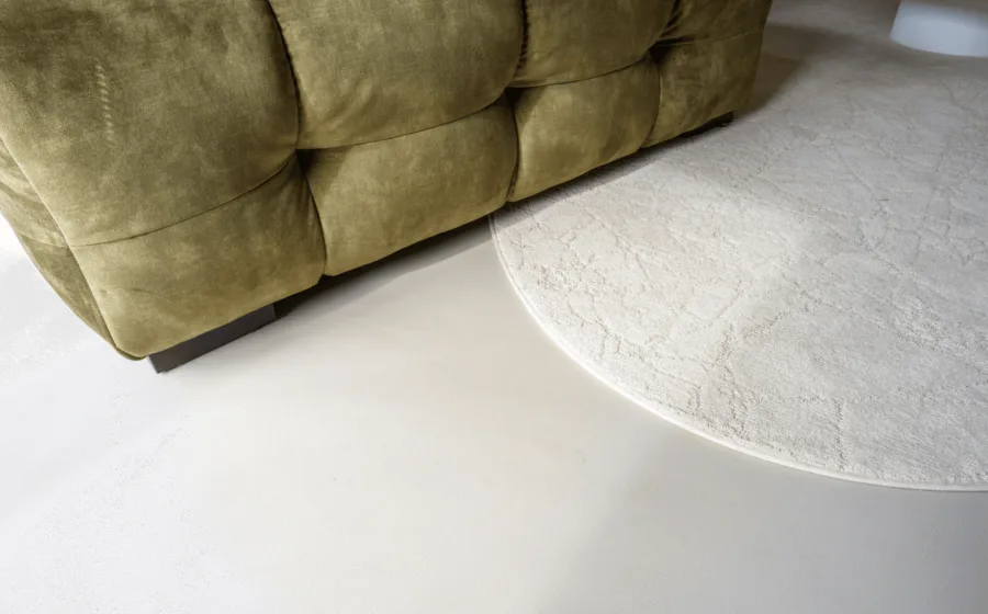 Licht grijze gietvloer met groene bank en organische, creme vloerkleed