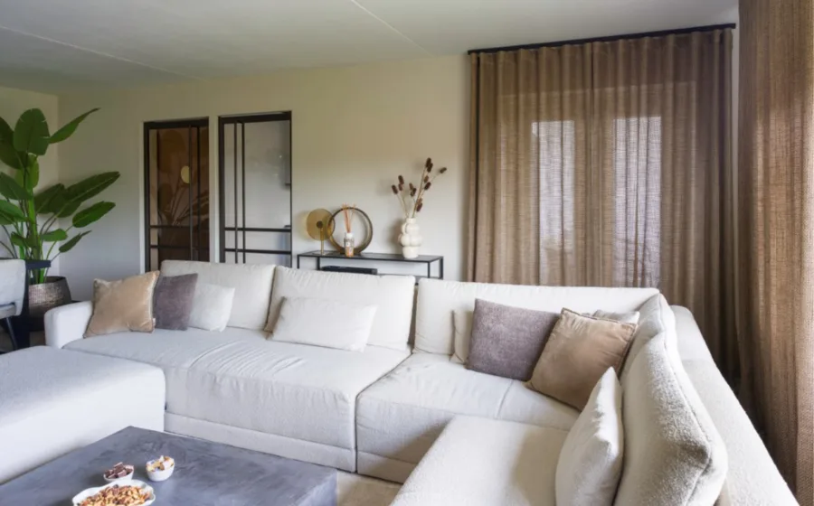 hotel chic woonkamer met bruine inbetweengordijnen, grijze u-bank en bronze stalen deuren