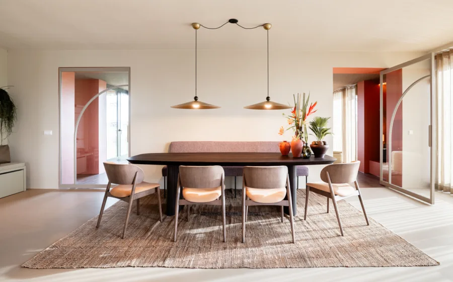 Eetkamer uit vtwonen Weer Verliefd op je Huis, aflevering 7 Landsmeer, met ovale houten tafel, vier stoelen, oudroze bank en messing hanglampen op een jute vloerkleed.