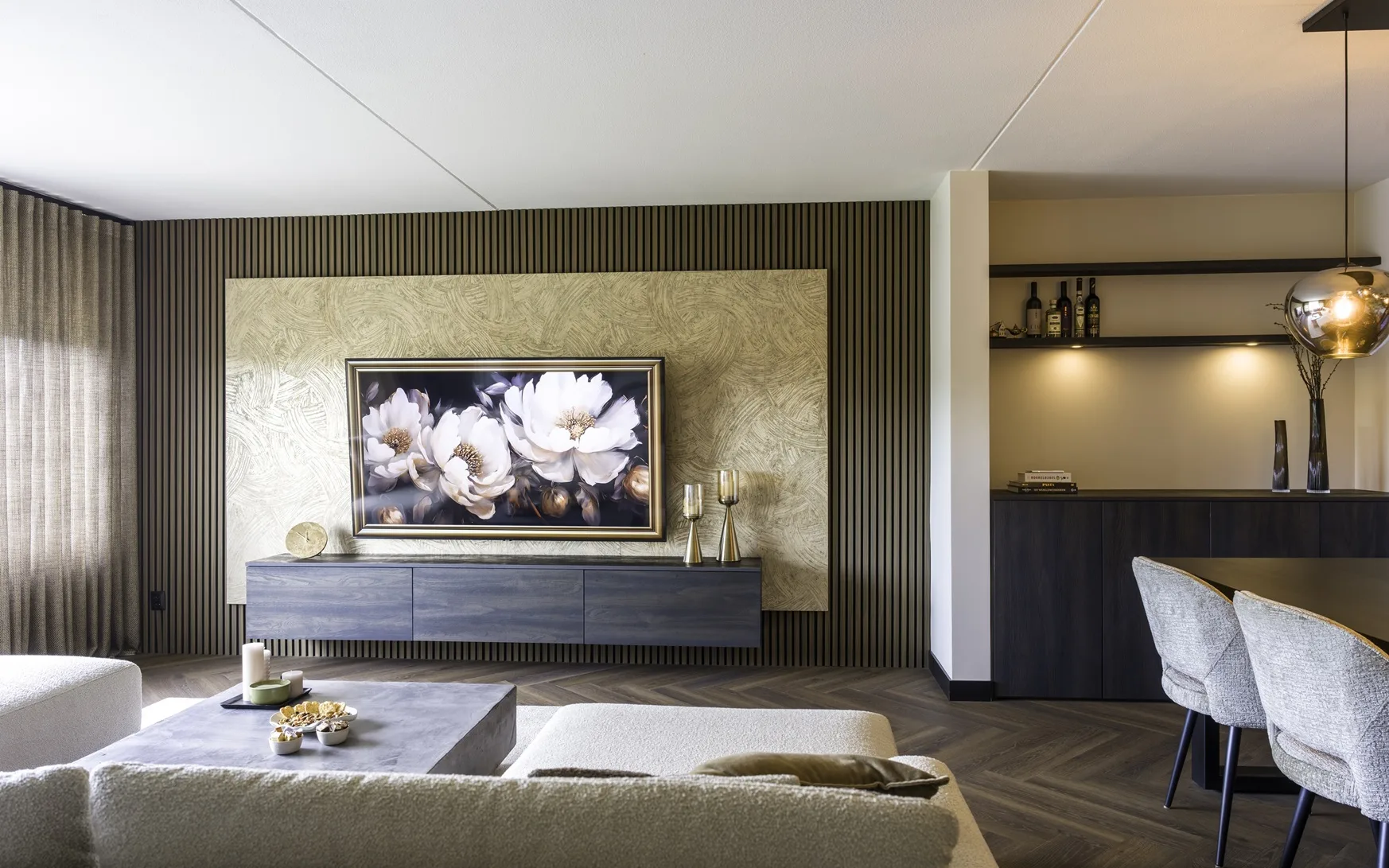 Hotel chique woonkamer met houten lattenwand, groot bloemenschilderij boven een zwevend dressoir, neutrale bank, betonnen salontafel en warme sfeerverlichting.