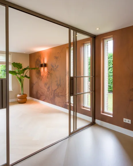 Brons kleurige stalen deuren met een houtvloer van Lindura in visgraat en een roestrode behang muur