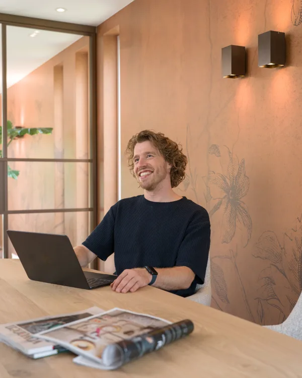 Man aan tafel met laptop voor muur met roestrood behang van Kek