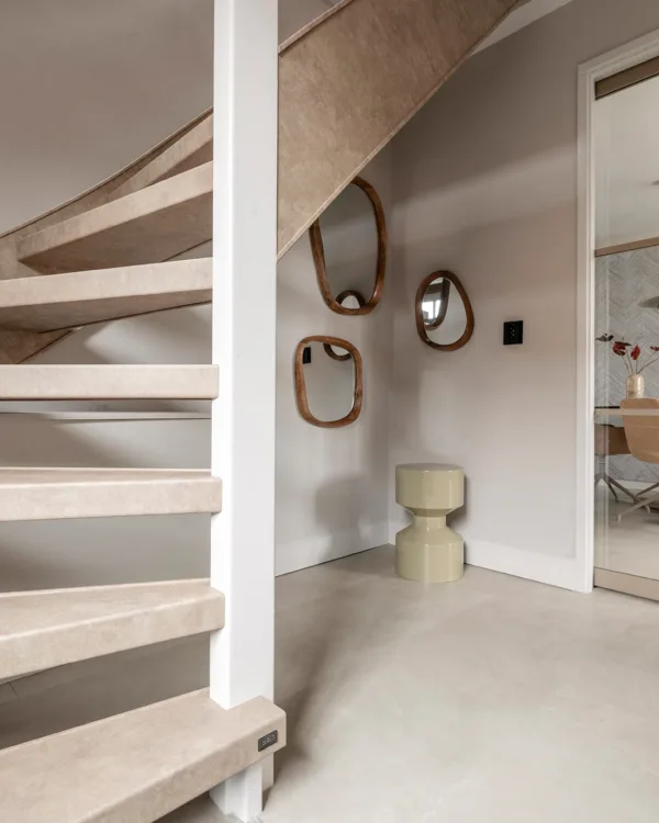 Hal met grijze betonlook vloer, open trap en witte muren
