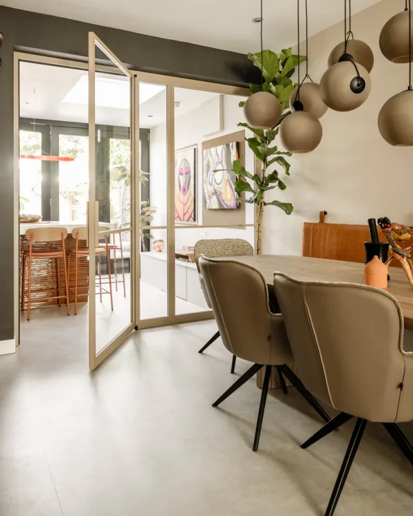 Keuken en woonkamer met lichtgrijze pvc tegelvloer, ovale eettafel en stalen deuren.