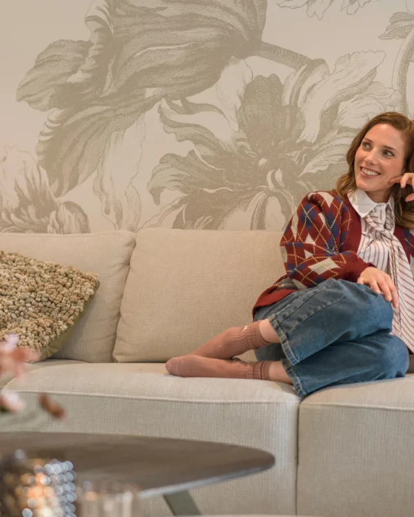 Vrouw op lichte bank met licht bloemen behang op de muur