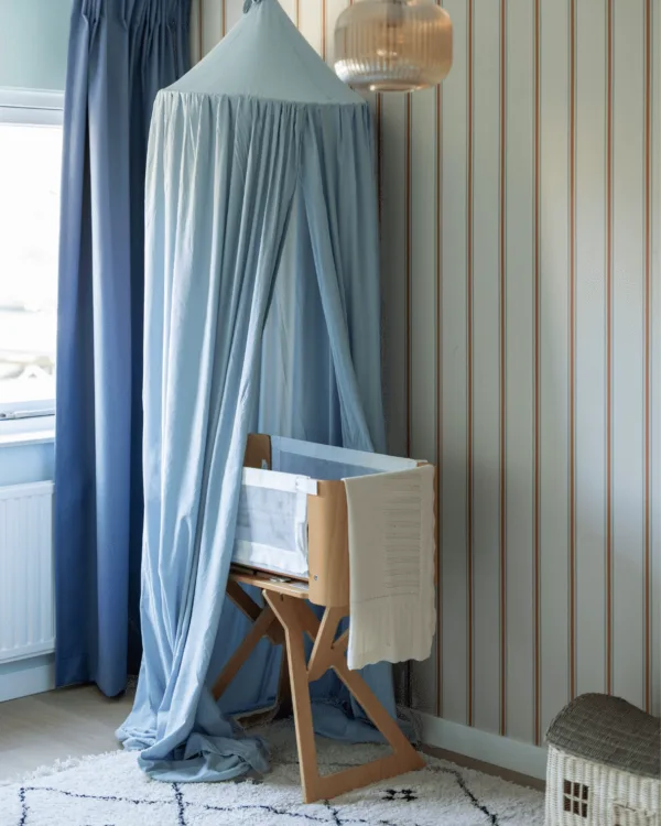 Blauw overgordijnen in babykamer met babyblauw klamboe en gestreept behang