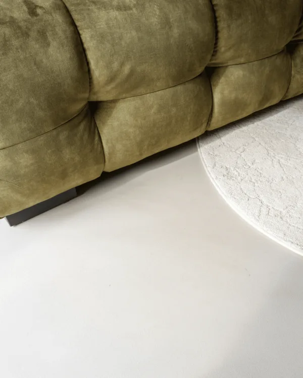 Grijze gietvloer met wit vloerkleed en groene bank