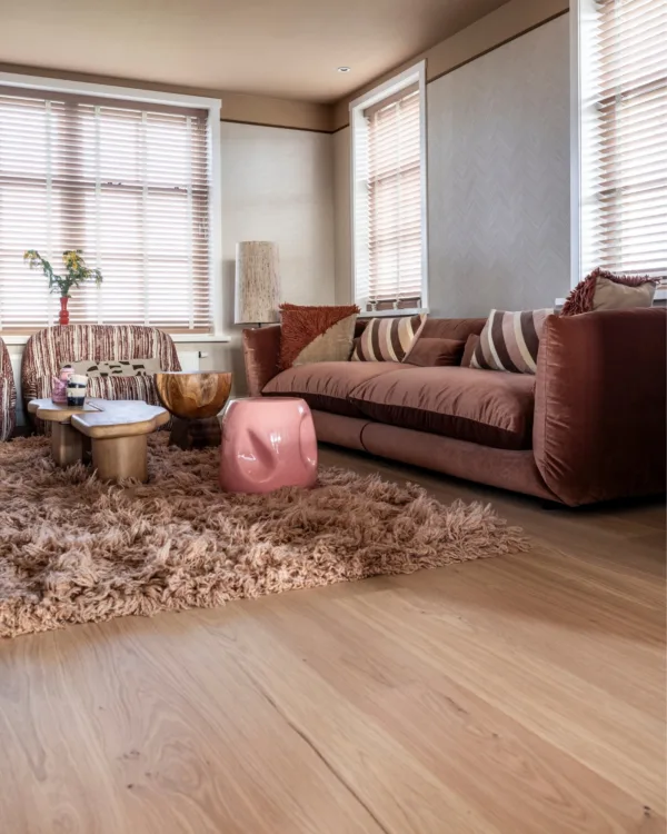 Warmkleurijke woonkamer met warme houten vloer, fluffy vloerkleed en houten jaloezieën