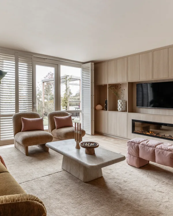 Woonkamer met wandkast op maat inclusief elektrische haard, fauteuils en witte shutters