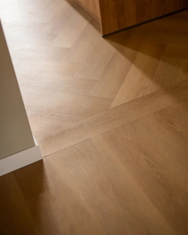 Visgraatvloer in de keuken loopt over in rechte houten planken in de woonkamer voor een subtiel contrast en eenheid.