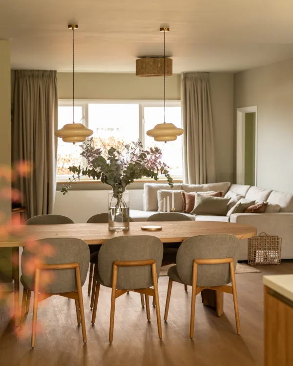 Gezellige woonkamer met rechte houten vloer, lichte inbetween gordijnen en natuurlijke materialen.