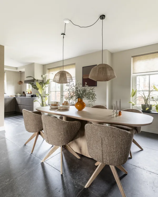Eetkamer met ovale 6persoons eettafel, kuipstoelen en grijze tegelvloer