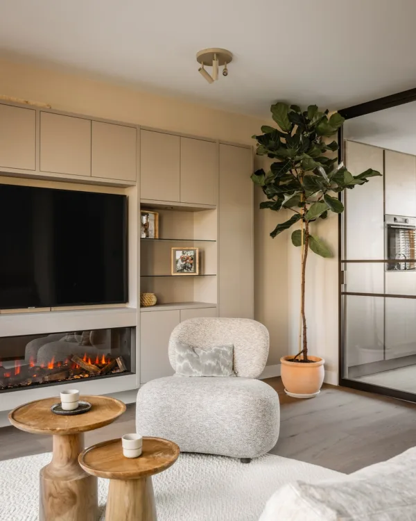 Woonkamer in natuurlijke tinten met beige fauteuil, kast op maat met elektrische haard en stalen deuren