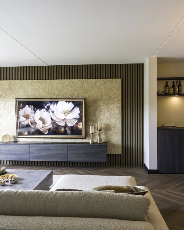 Hotel chique woonkamer met houten lattenwand, groot bloemenschilderij boven een zwevend dressoir, neutrale bank, betonnen salontafel en warme sfeerverlichting.