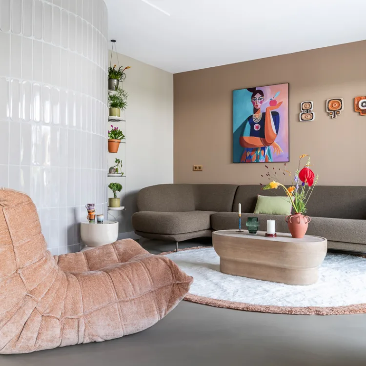 Woonkamer met gezellige hoekbank, rond vloerkleed en relax stoel in natuurlijke tinten voor een rustig en stijlvol interieur.