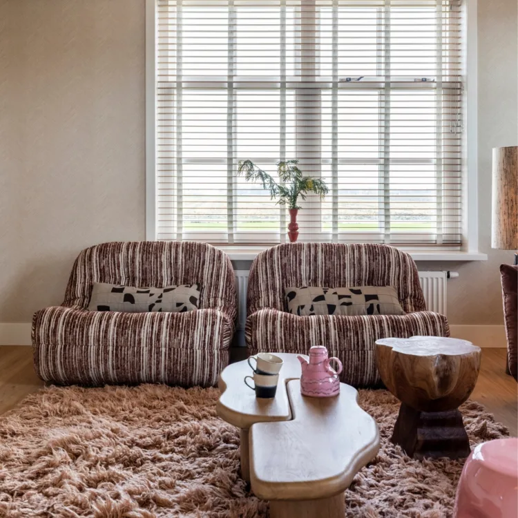 Warmkleurijke woonkamer met warme houten vloer, fluffy vloerkleed en houten jaloezieën