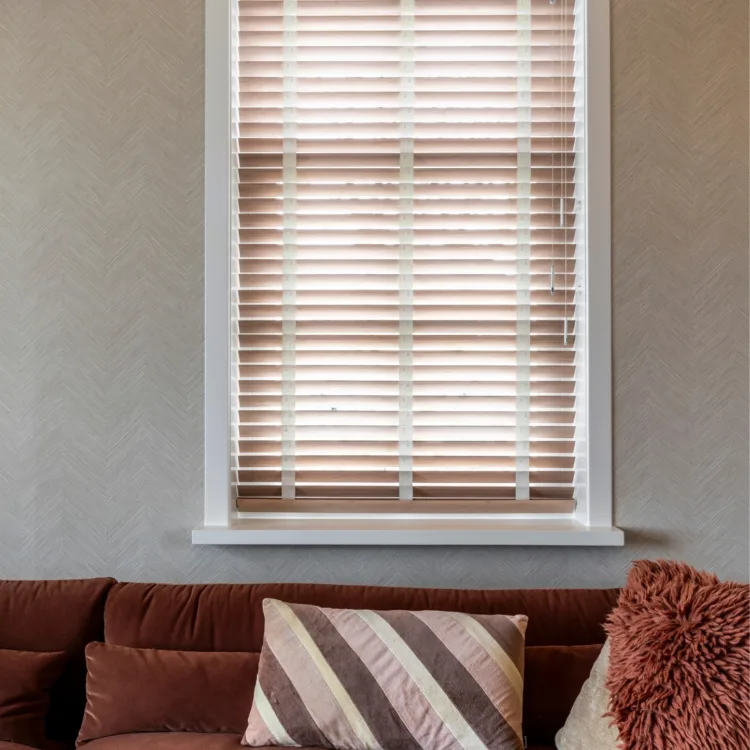 Warmkleurijke woonkamer met houten jaloezieën en donker rode bank