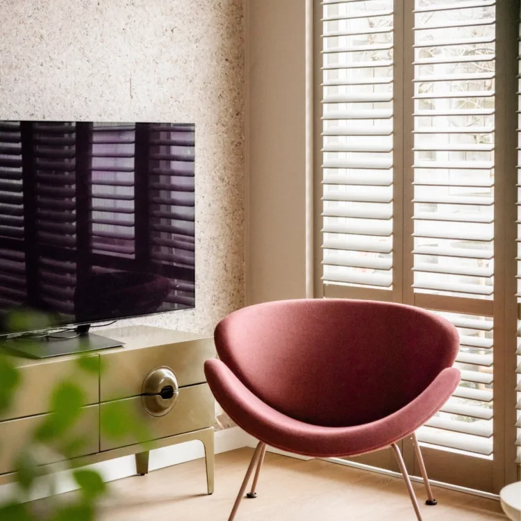 Warm kleurrijke woonkamer met lichte houtlook pvc-vloer, vloerkleed en witte shutters