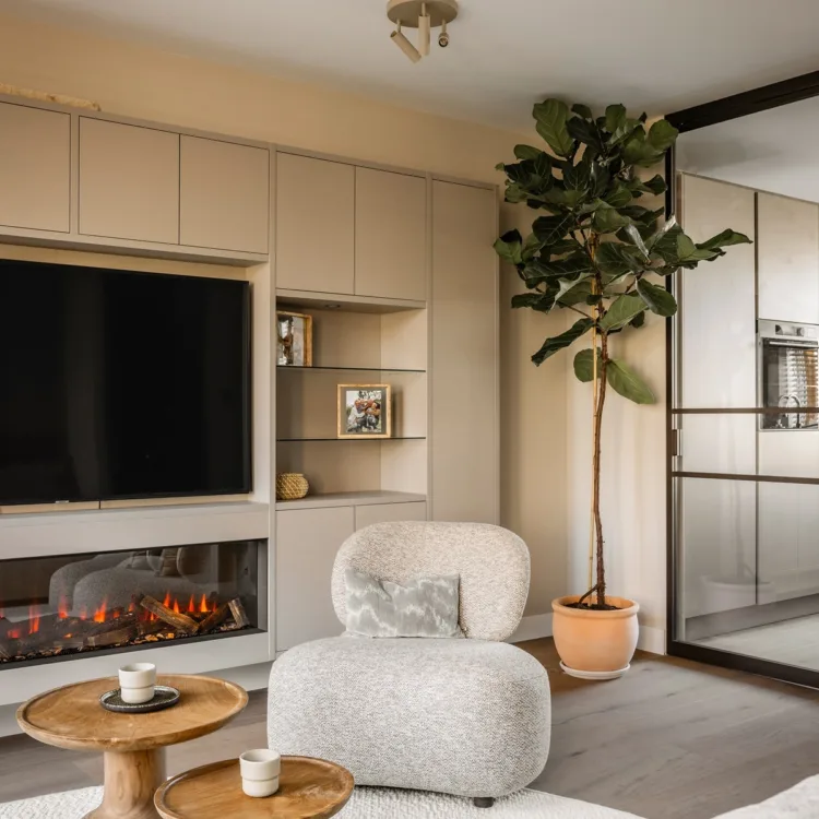Woonkamer in natuurlijke tinten met beige fauteuil, kast op maat met elektrische haard en stalen deuren