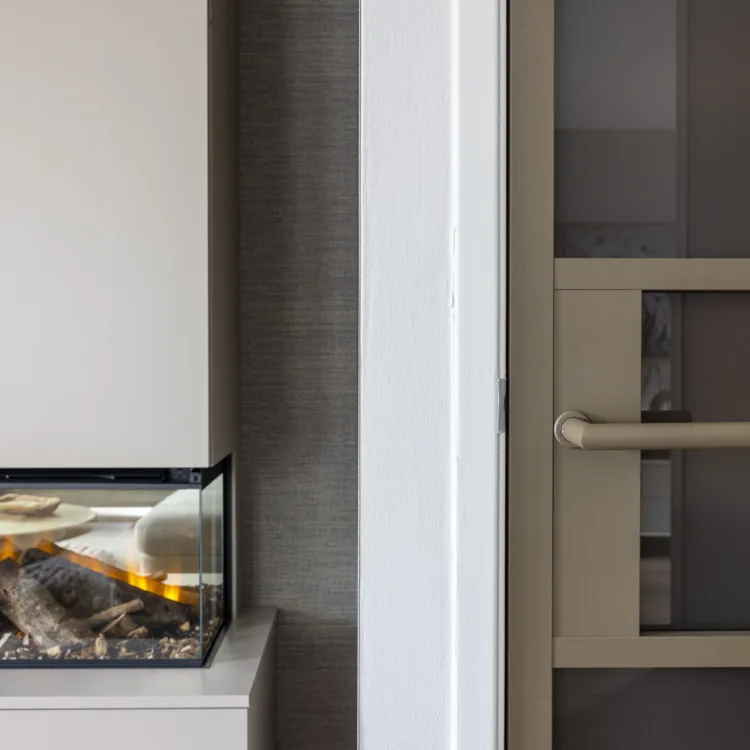 Hotel chique detail met moderne inbouwhaard achter glas, strakke maatwerkkast en taupe binnendeur met matglas en bijpassende greep.