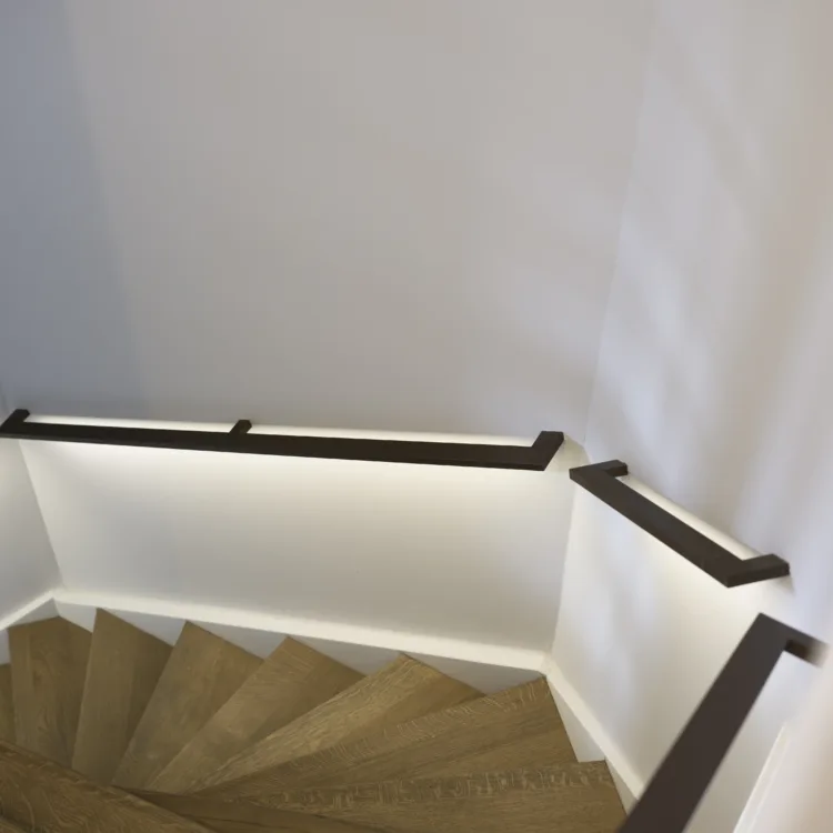 Hotel chique trapopgang met visgraat houten treden, strakke witte wanden en minimalistische zwarte leuningen met indirecte verlichting.