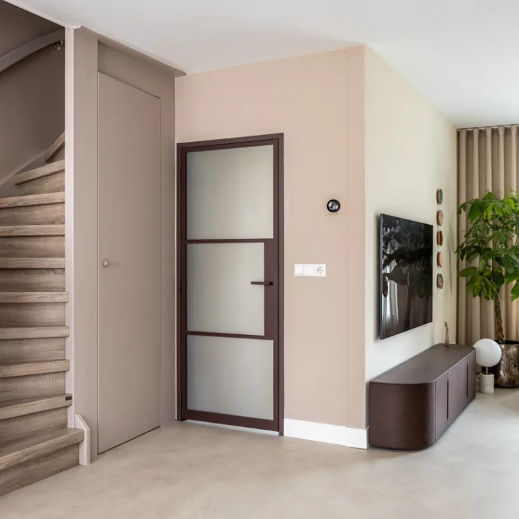PVC-vloer in betonlook in een lichte, moderne woonkamer met een open trap en stalen binnendeur.