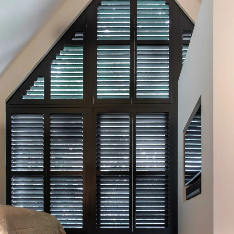 Zwarte shutters op maat voor hoge ramen met een schuine vorm.