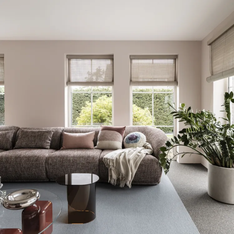 Woonkamer met grote hoekbank en geweven hout raamdecoratie in lichte beigetint