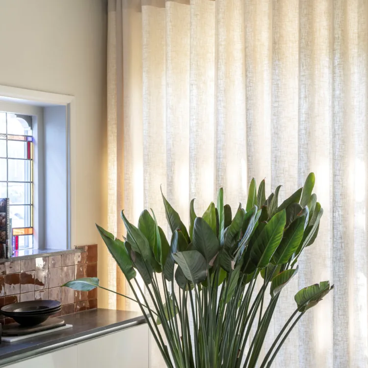 lange ware gordijnen in een beige tint met een plant ervoor